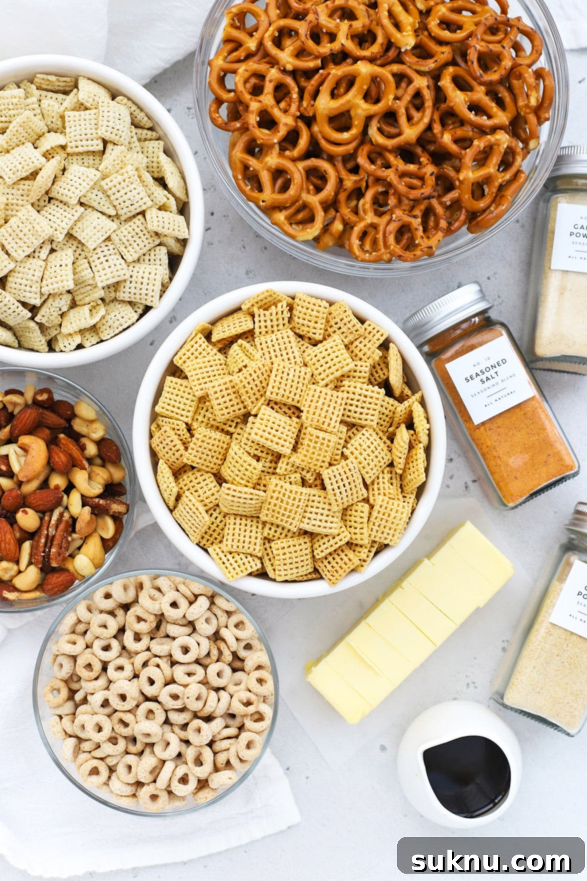 Overhead view of various gluten-free Chex Mix ingredients laid out on a white background, including cereals, pretzels, and nuts.