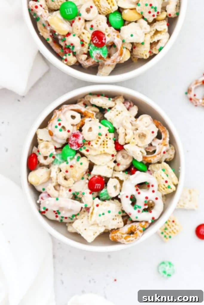 Two white bowls of gluten-free Christmas Chex mix with M&Ms and pretzels, perfect for holiday snacking.
