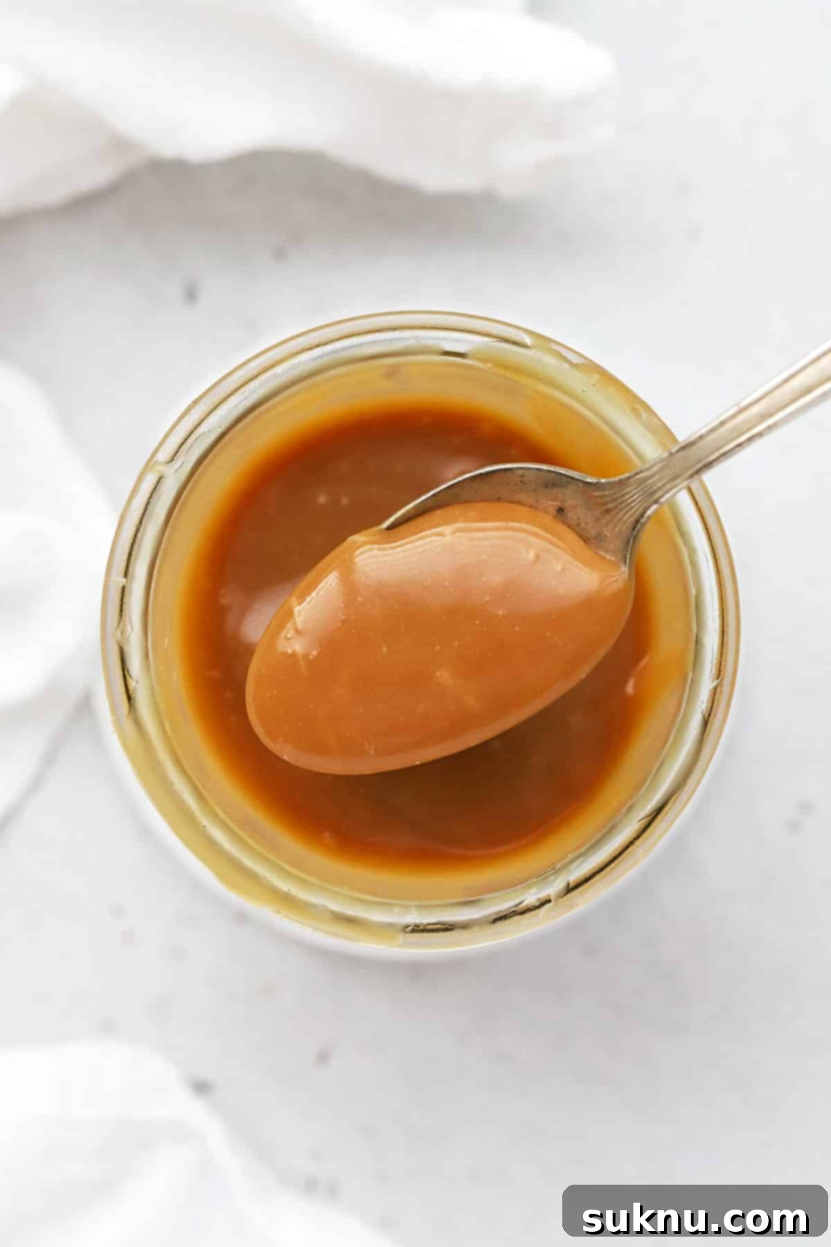 A spoonful of easy homemade caramel sauce being scooped, glistening and rich.
