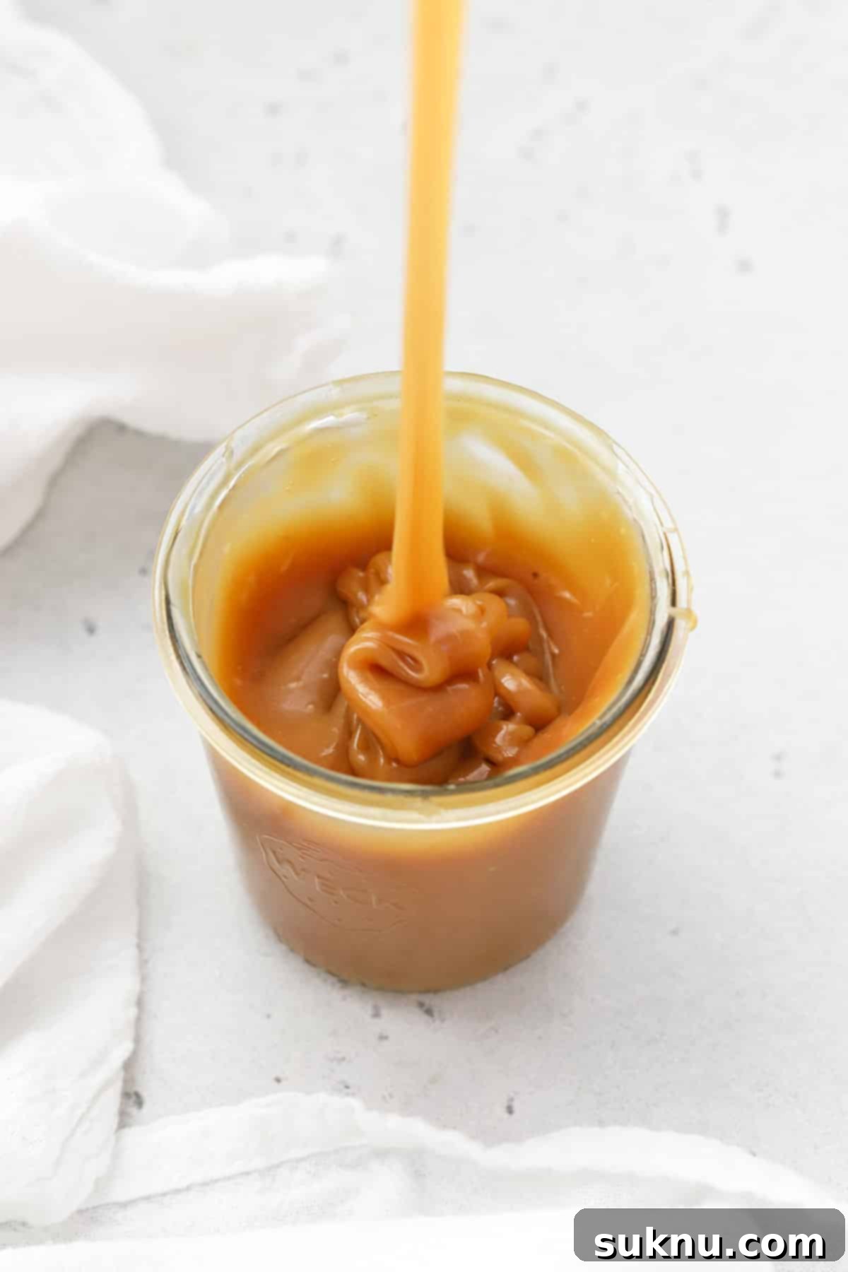 Pouring thick homemade caramel sauce into a jar, highlighting its luxurious texture.