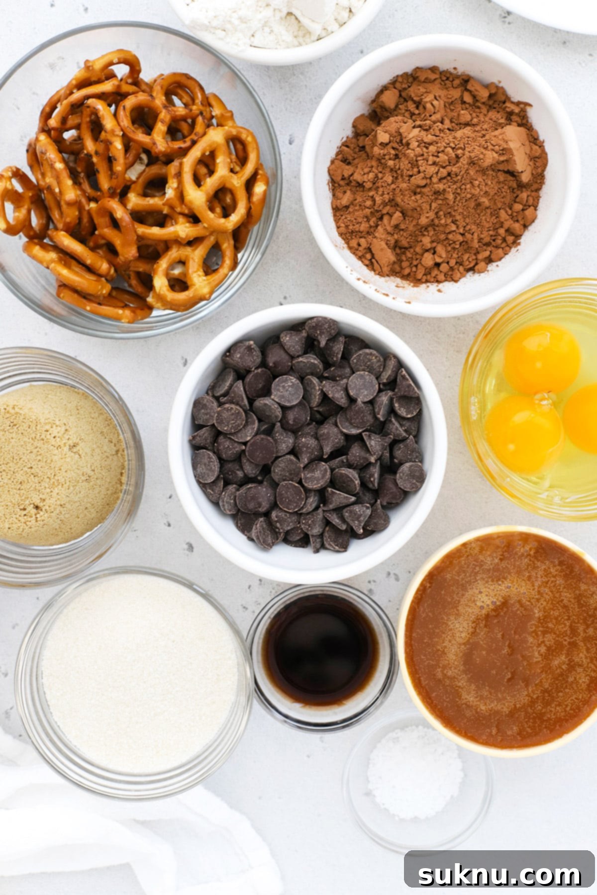 Overhead view of meticulously laid out ingredients for crafting gluten-free caramel pretzel brownies, including chocolate chips, flour, sugar, butter, and pretzels.