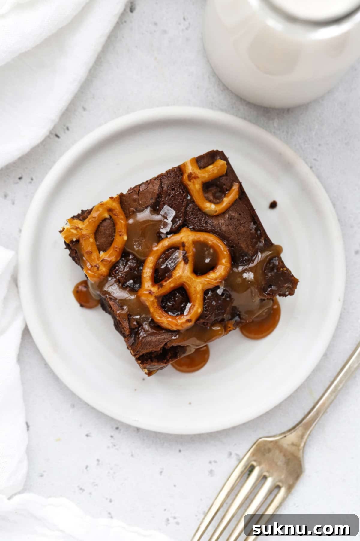 A single, perfectly cut gluten-free caramel pretzel brownie served on a white plate, ready to be enjoyed.