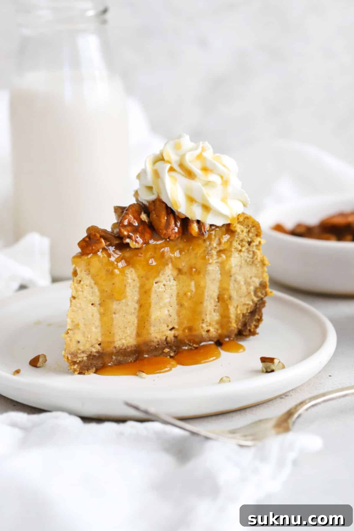 front view of a slice of gluten-free pumpkin cheesecake topped with toasted pecans, caramel sauce and whipped cream