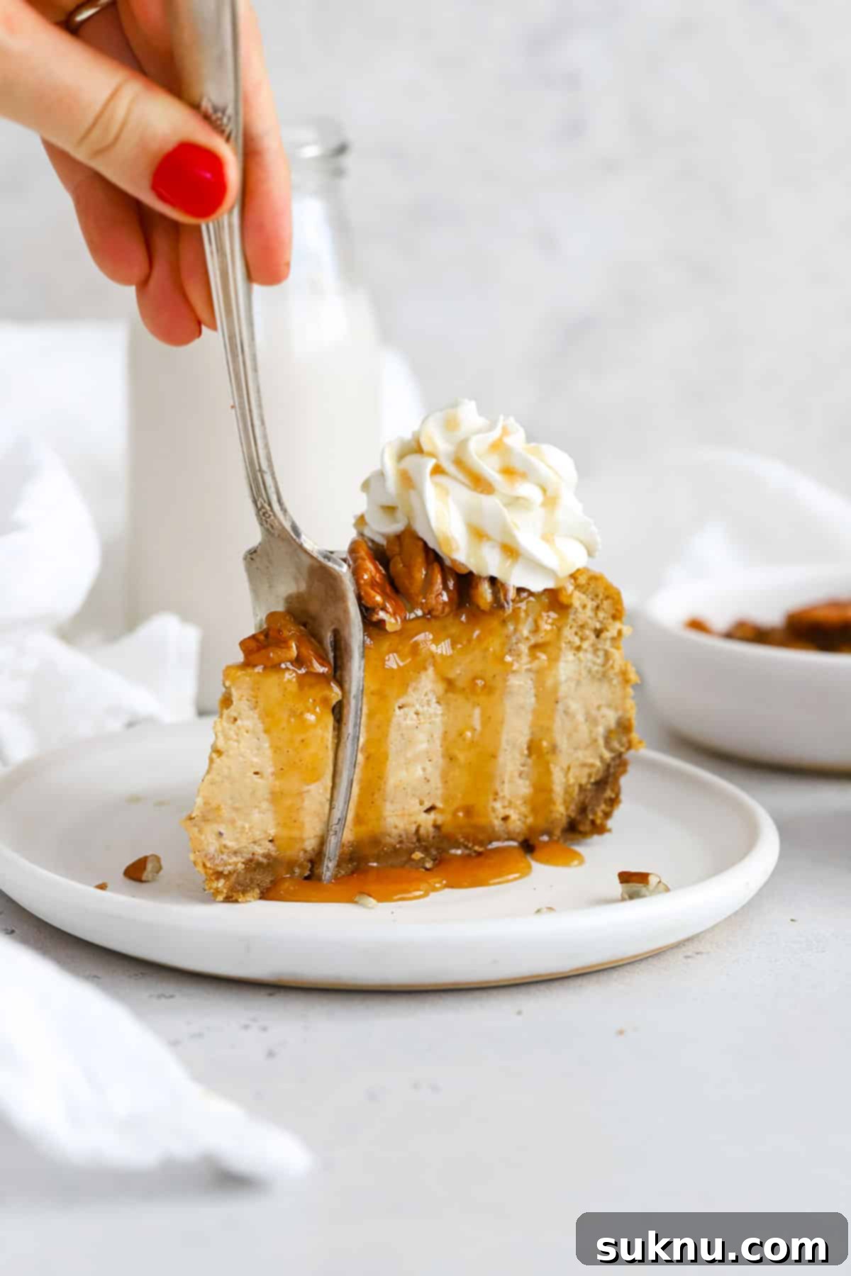 front view of a slice of gluten-free pumpkin cheesecake topped with toasted pecans, caramel sauce and whipped cream