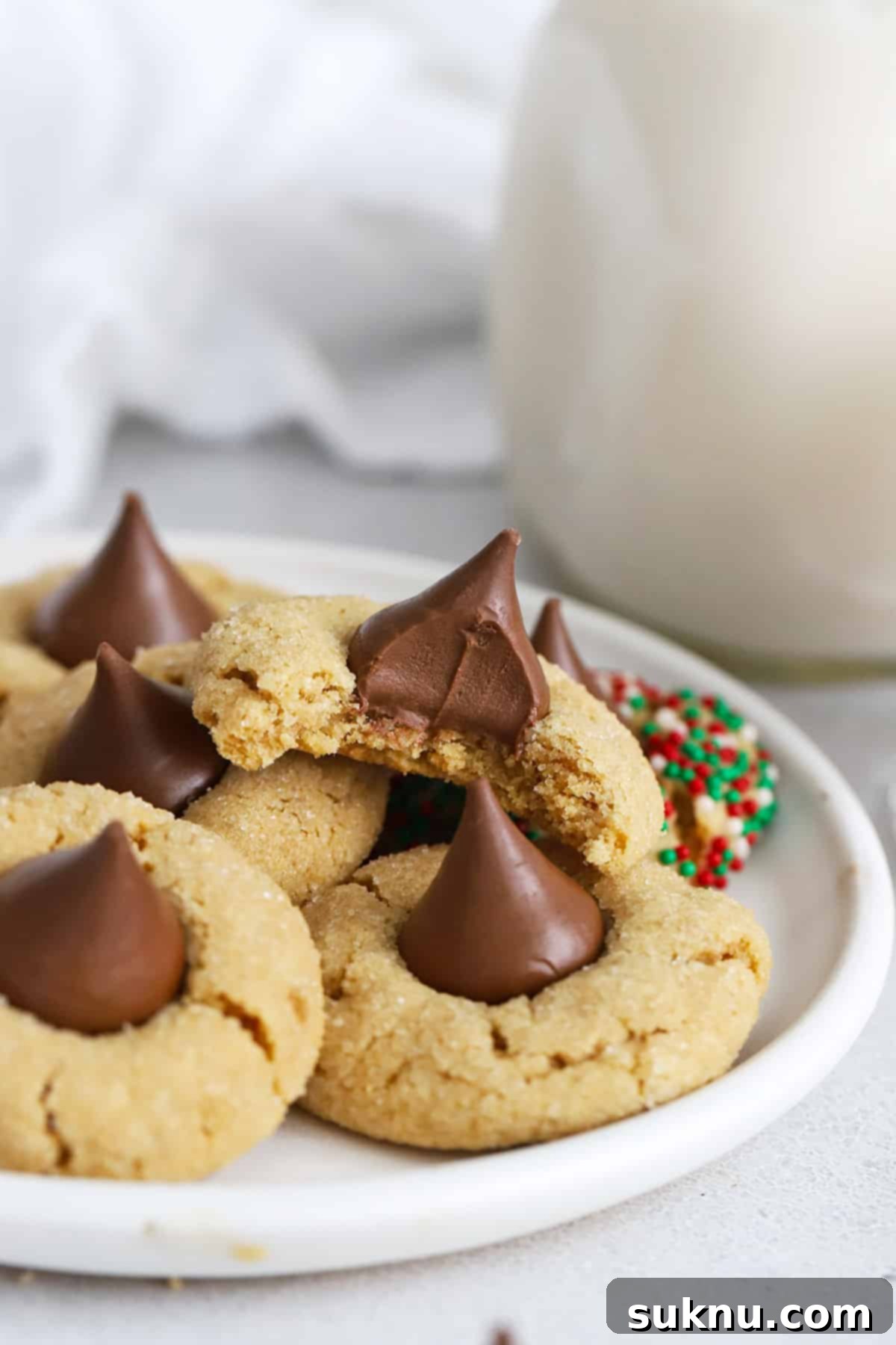 A plate stacked with gluten-free peanut butter blossom cookies. One has a bite out of it, revealing a soft, chewy texture.