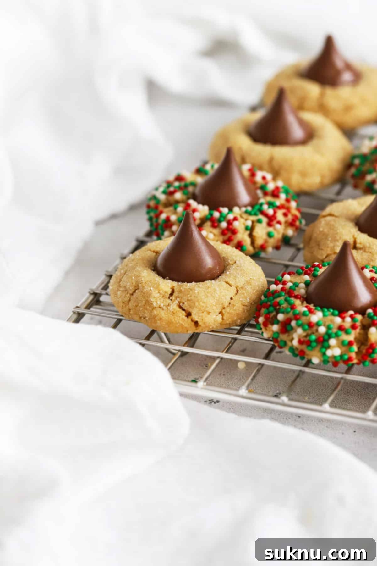 Gluten-free peanut butter blossoms cooling on a wire rack. some are rolled in red and green nonpareil sprinkles.
