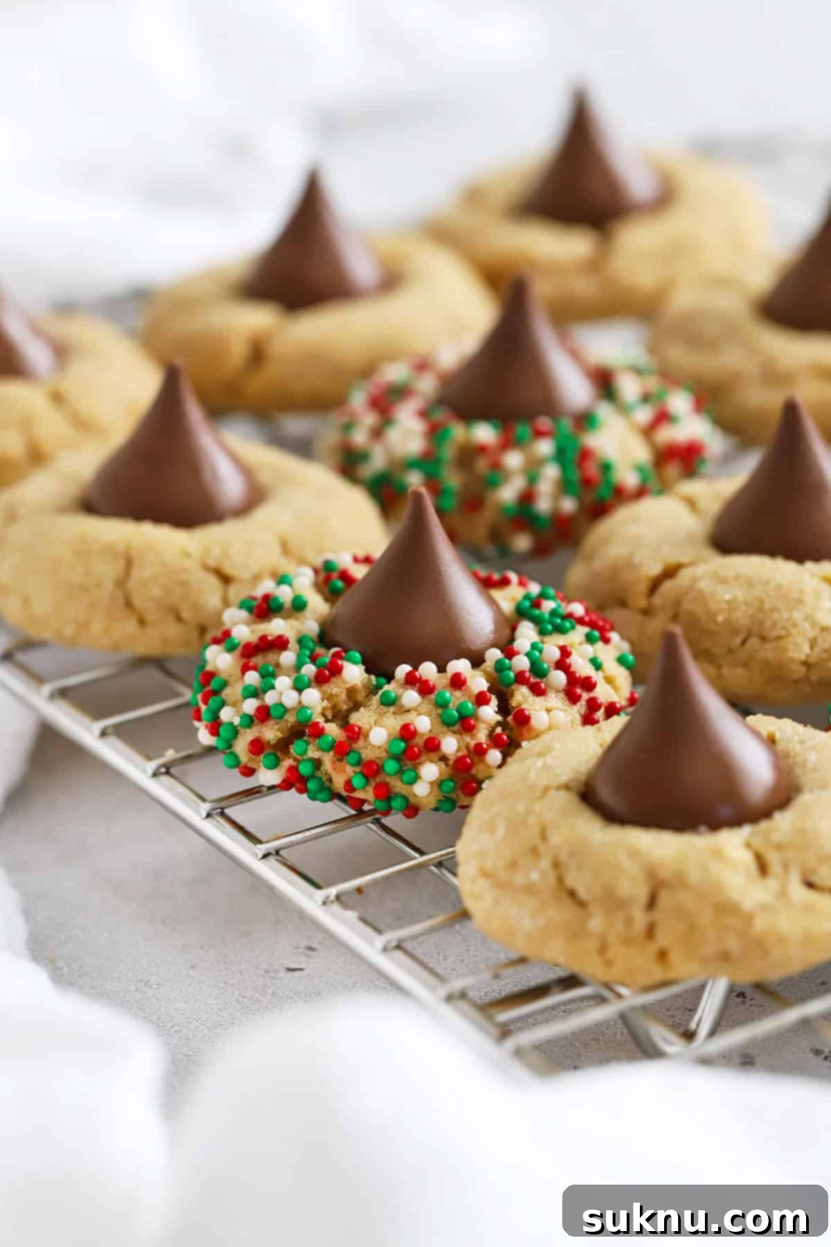 Gluten-free peanut butter blossoms cooling on a wire rack. some are rolled in red and green nonpareil sprinkles.