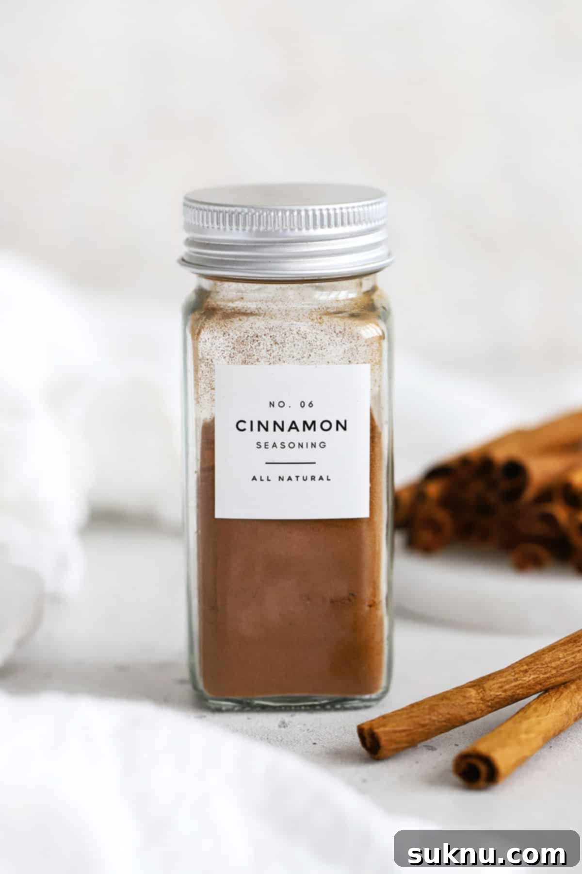 Front view of a jar of ground cinnamon with cinnamon sticks in the background