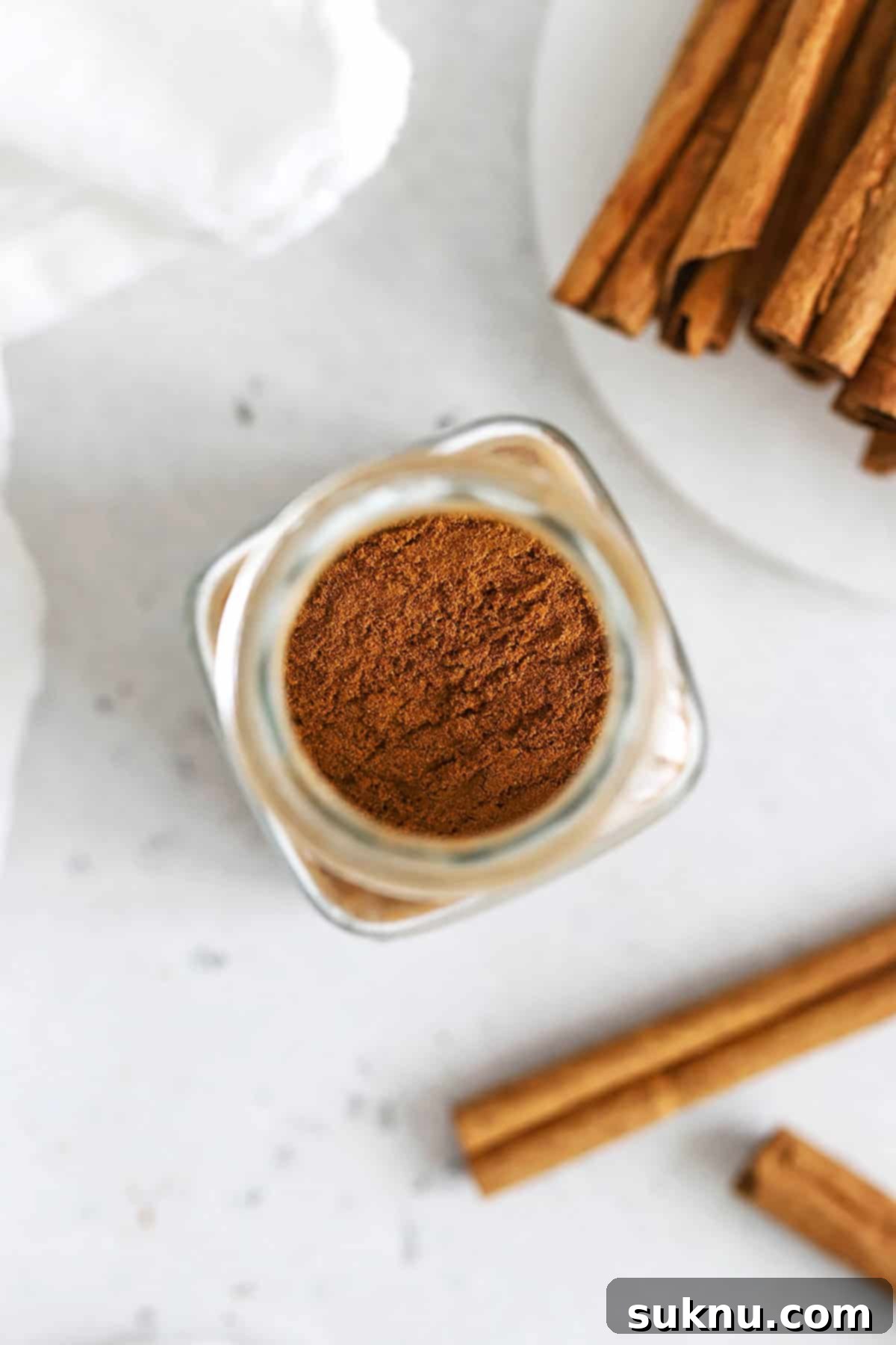Overhead view into a jar of ground cinnamon with cinnamon sticks in the background