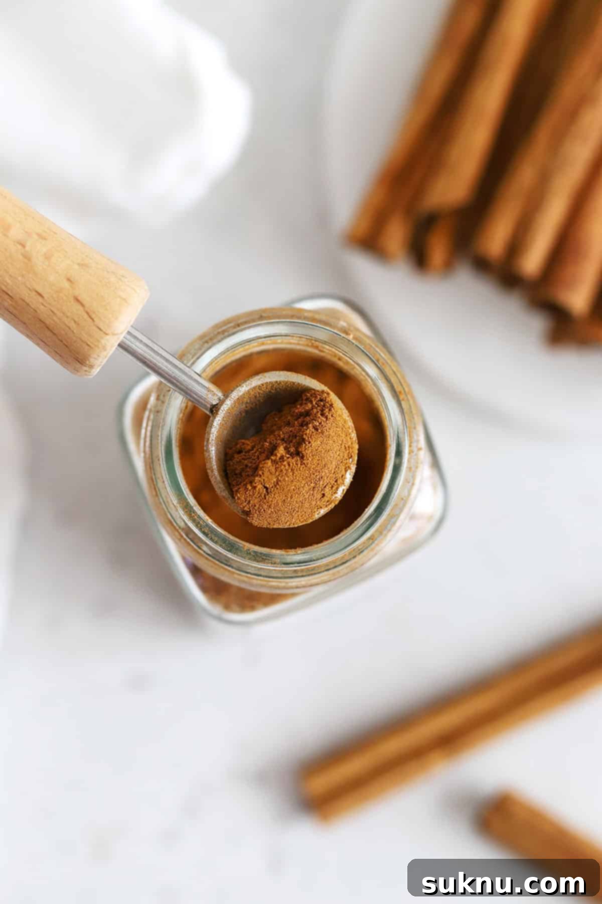 Overhead view into a jar of ground cinnamon with cinnamon sticks in the background