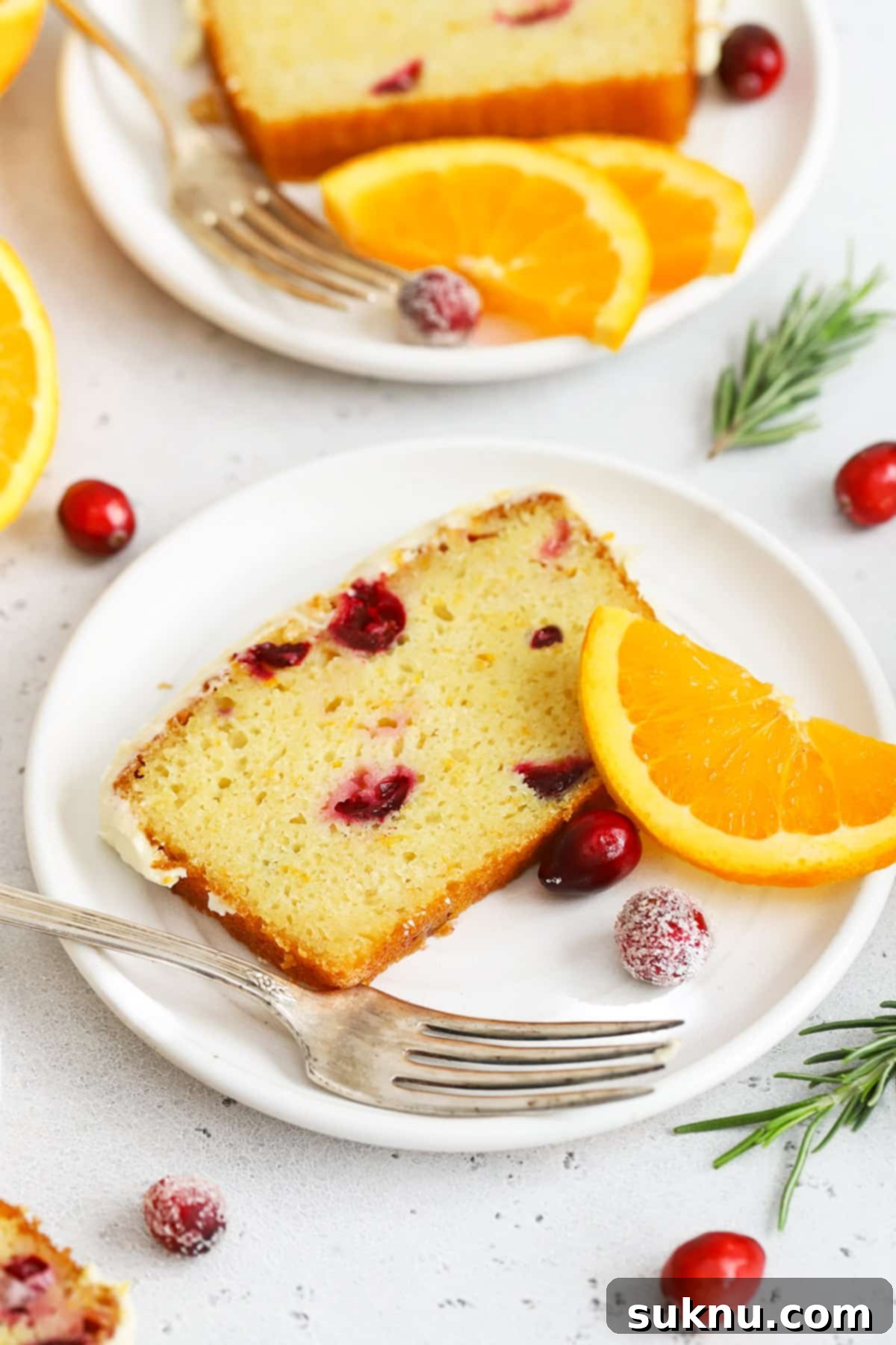 Front view of a slice of gluten-free orange cranberry loaf cake on a white plate with sugared cranberries