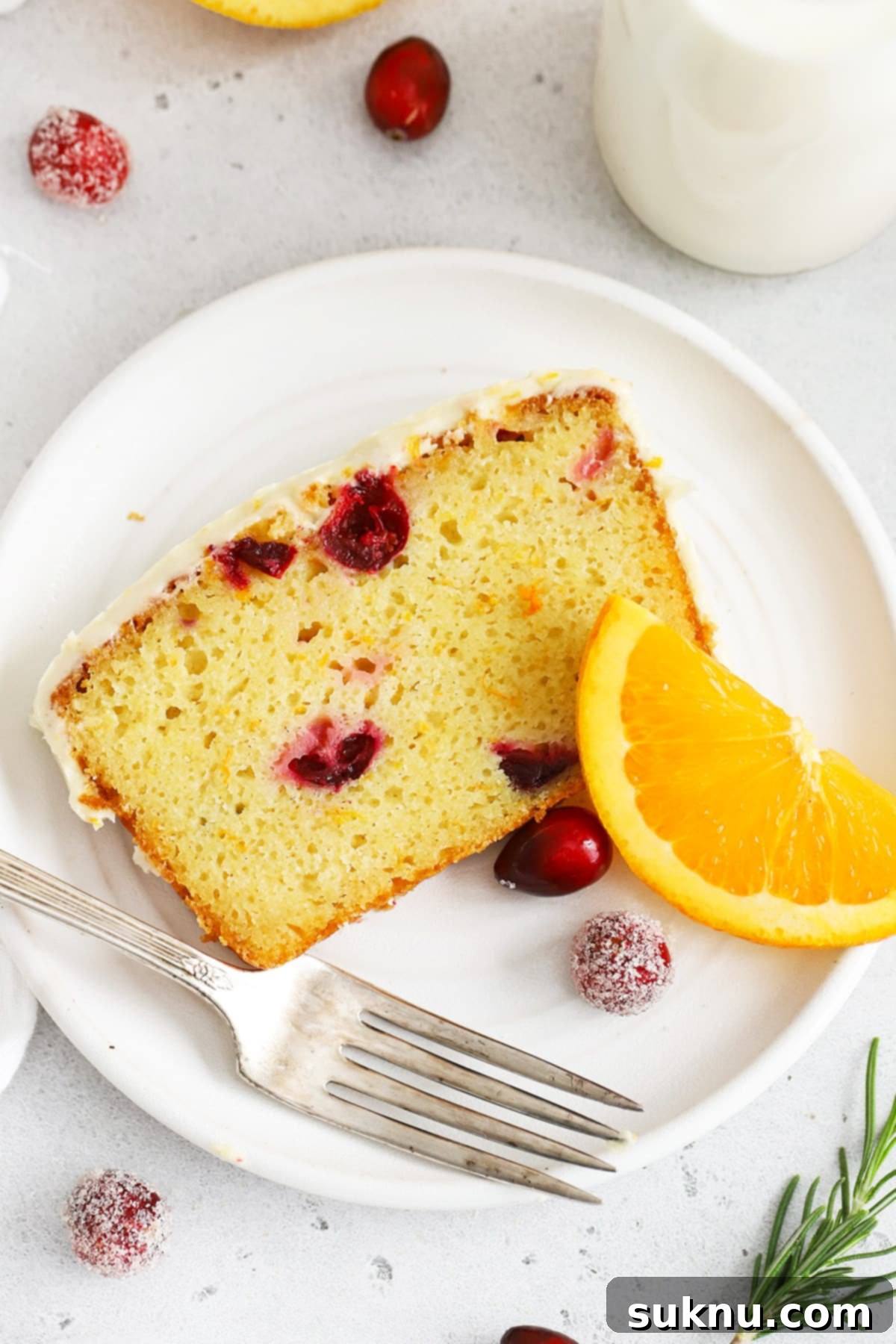 Overhead view of a slice of gluten-free orange cranberry loaf cake on a white plate with sugared cranberries