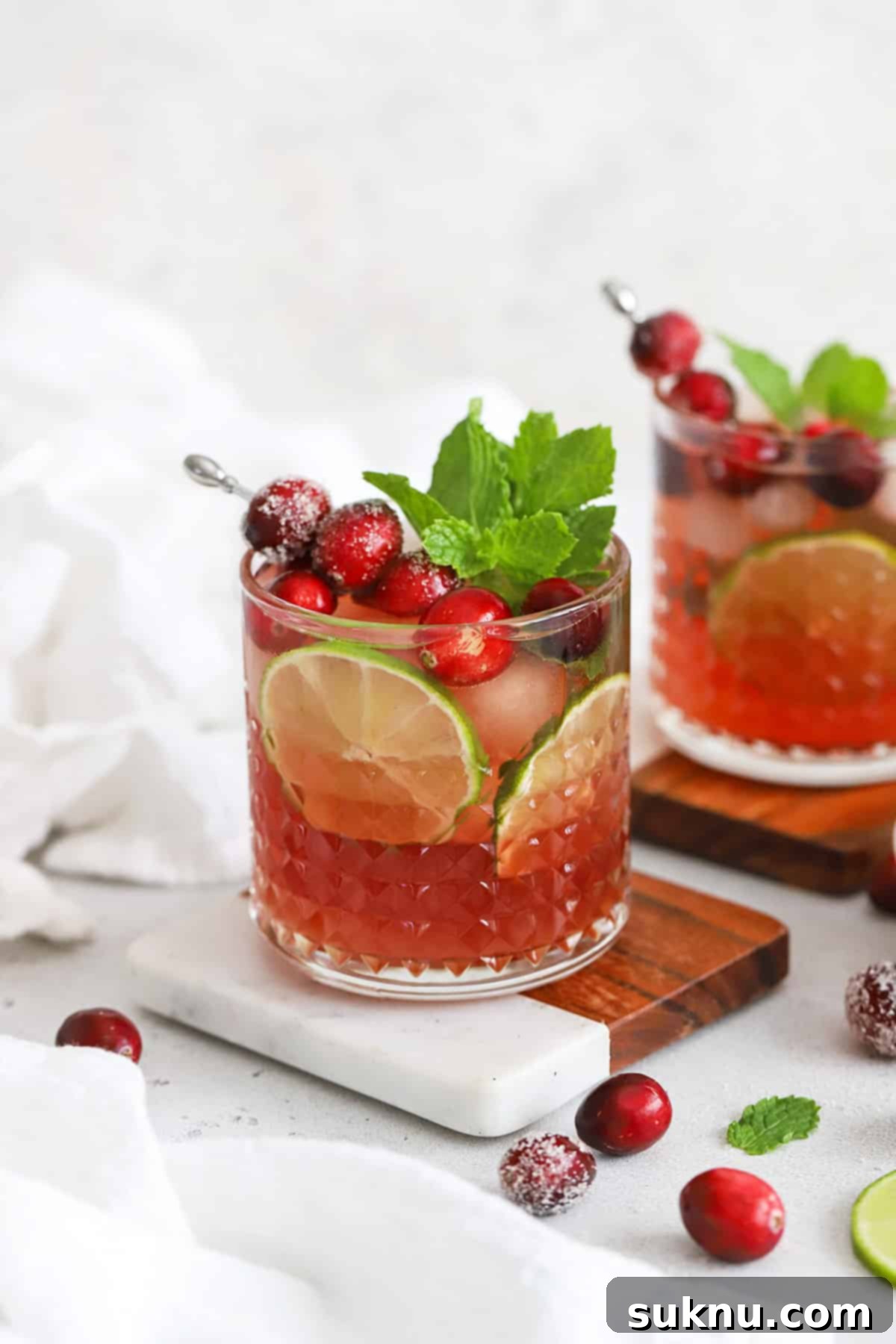 Sparkling Cranberry Lime Delight 2 Front view of cranberry lime mocktails in embossed glasses topped with sugared cranberries, lime slices, and fresh mint