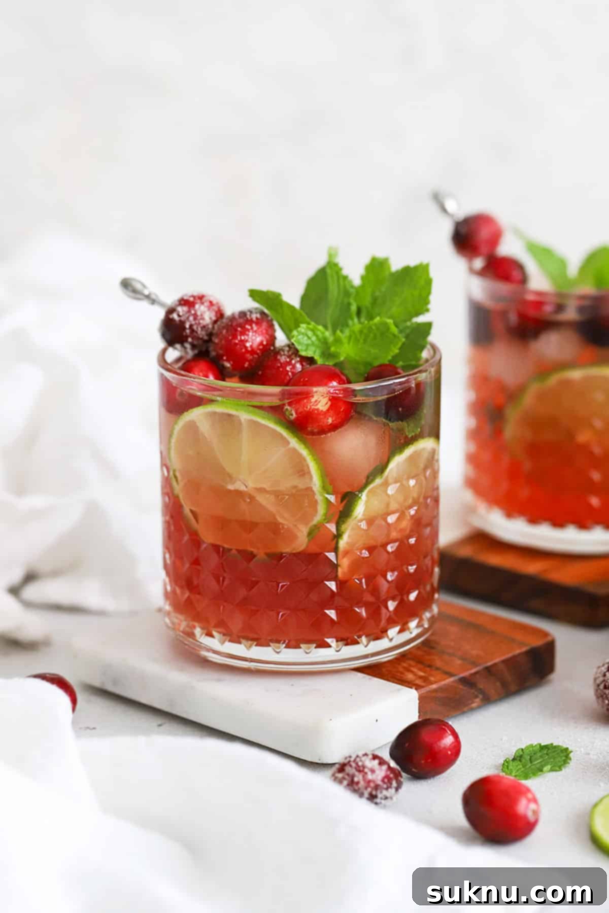 Sparkling Cranberry Lime Delight 14 Front view of cranberry lime mocktails in embossed glasses topped with sugared cranberries, lime slices, and fresh mint