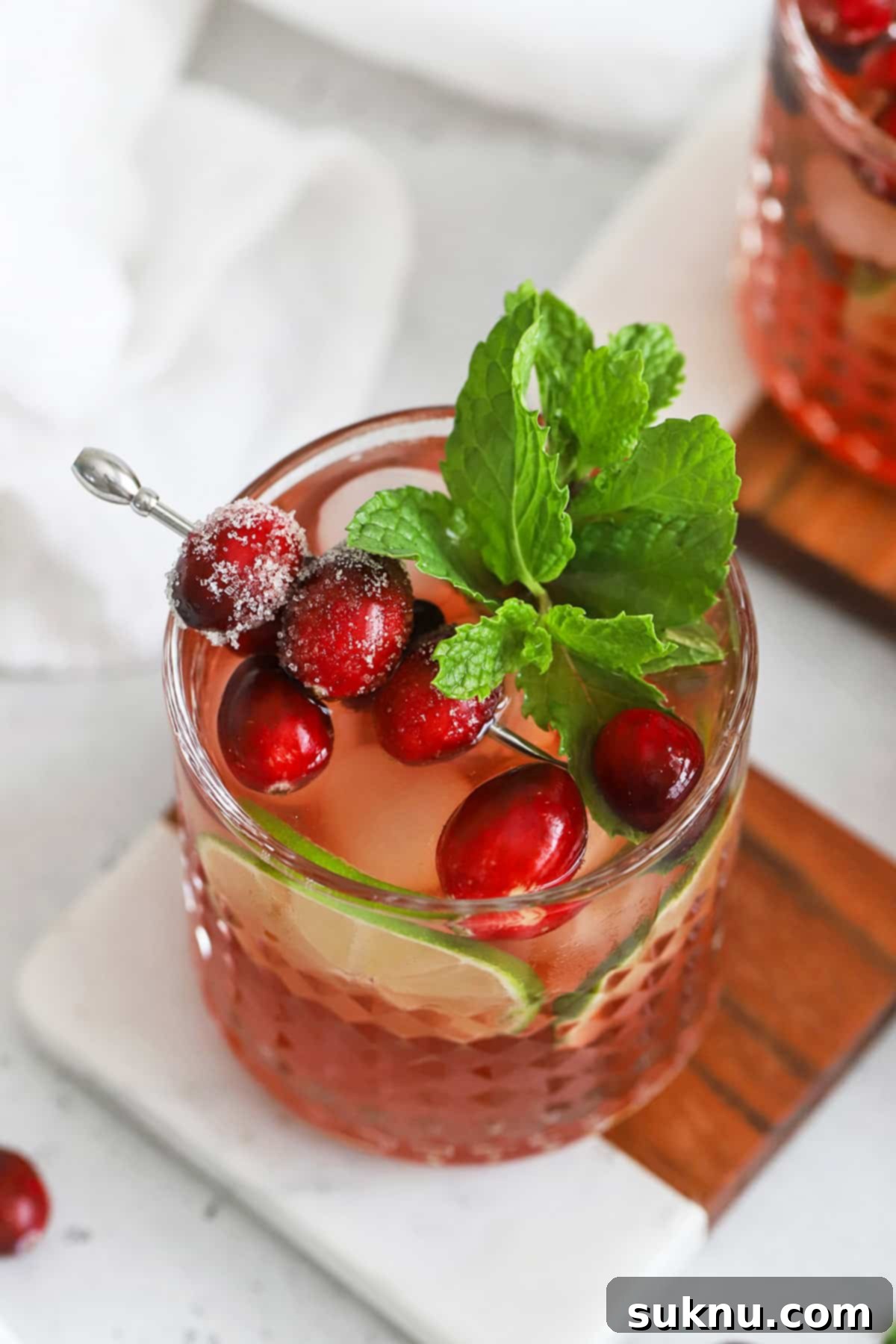 Sparkling Cranberry Lime Delight 6 Overhead view of a cranberry mocktail in an embossed glass topped with sugared cranberries, lime slices, and a sprig of fresh mint