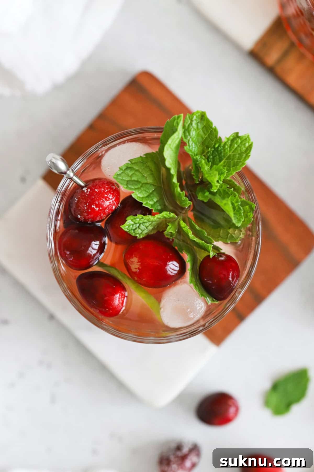 Sparkling Cranberry Lime Delight 7 Overhead view of a cranberry mocktail in an embossed glass topped with sugared cranberries, lime slices, and a sprig of fresh mint