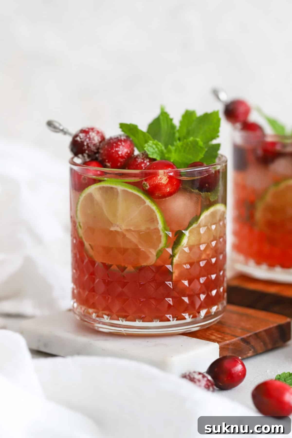 Sparkling Cranberry Lime Delight 8 Front view of cranberry lime mocktails in embossed glasses topped with sugared cranberries, lime slices, and fresh mint