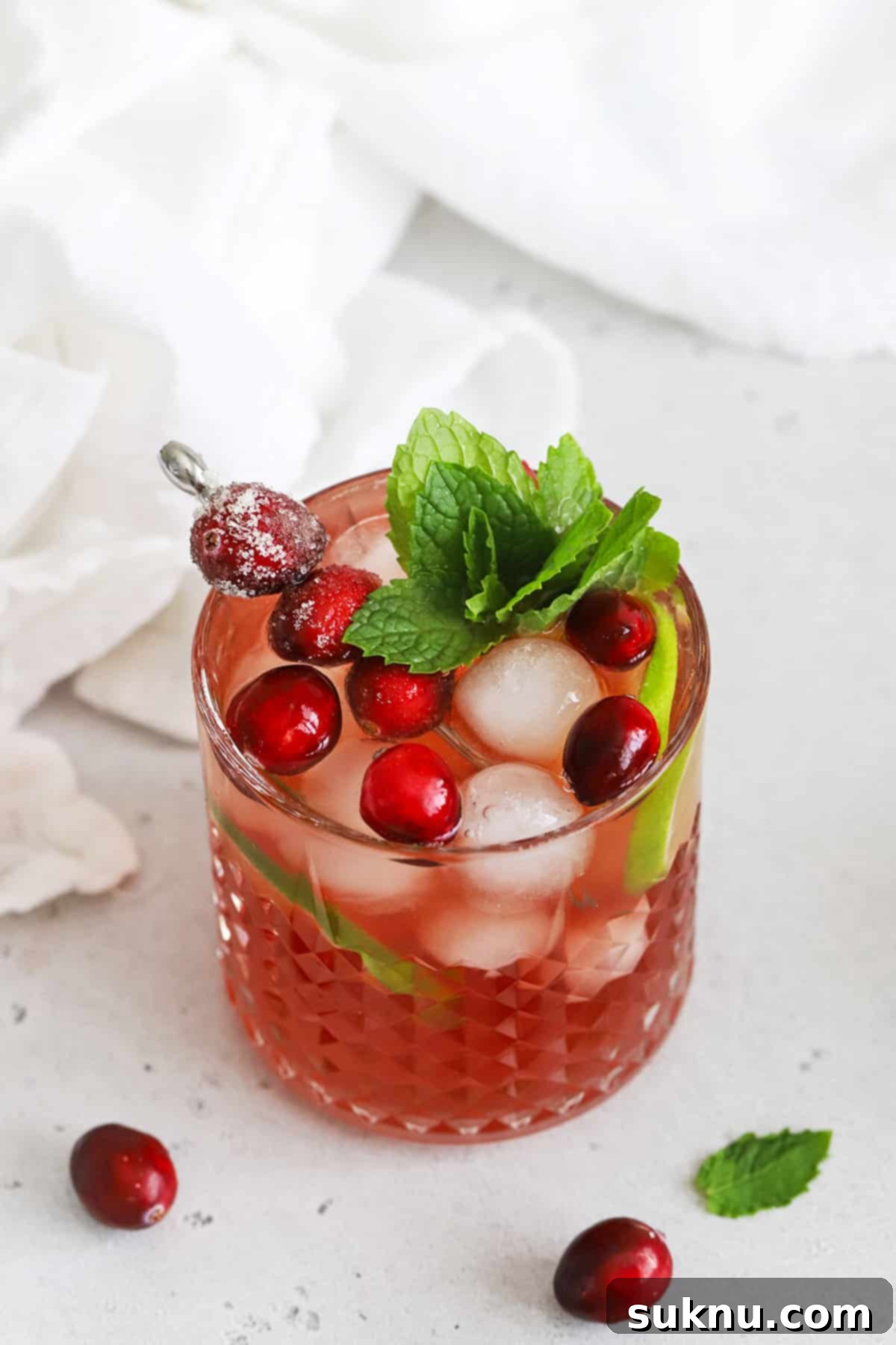 Sparkling Cranberry Lime Delight 9 Overhead view of a cranberry mocktail in an embossed glass topped with sugared cranberries, lime slices, and a sprig of fresh mint
