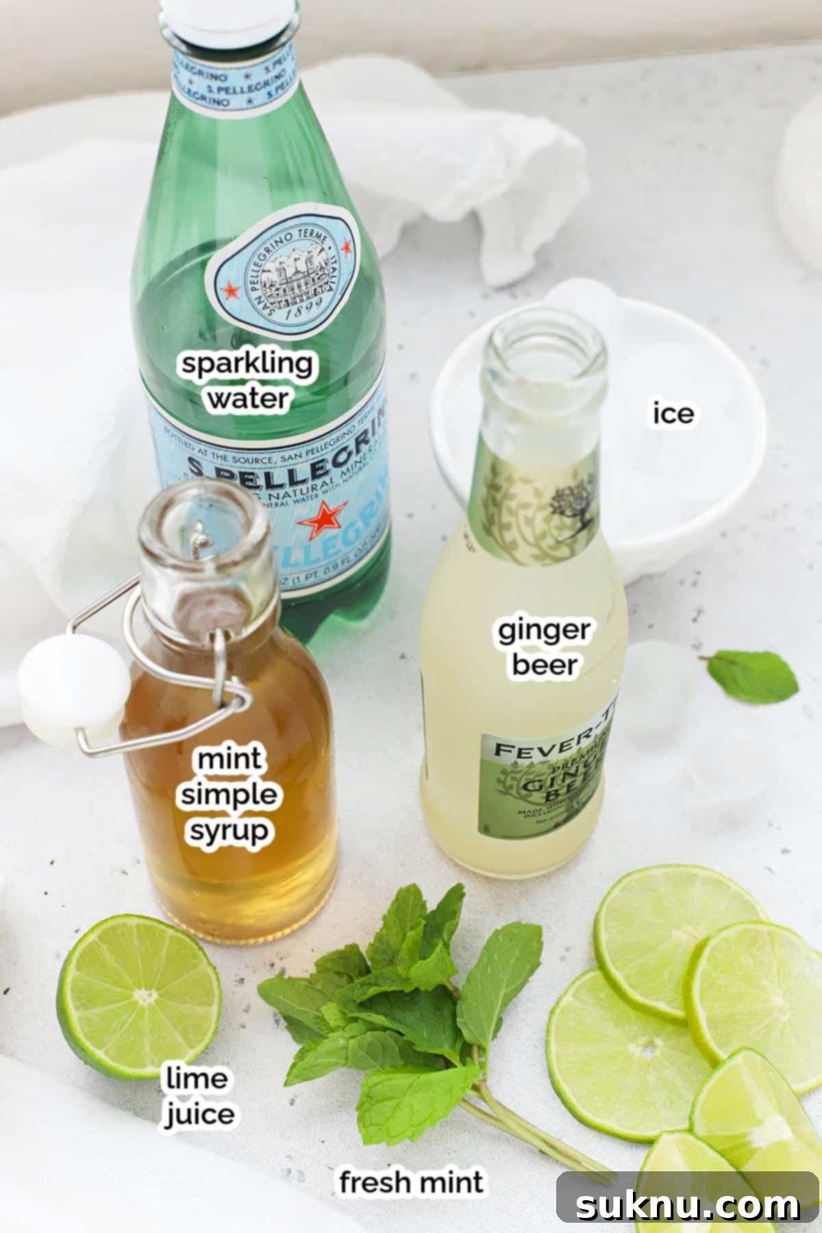 Ingredients for virgin Moscow Mule mocktails laid out, including limes, mint, ginger beer, and simple syrup