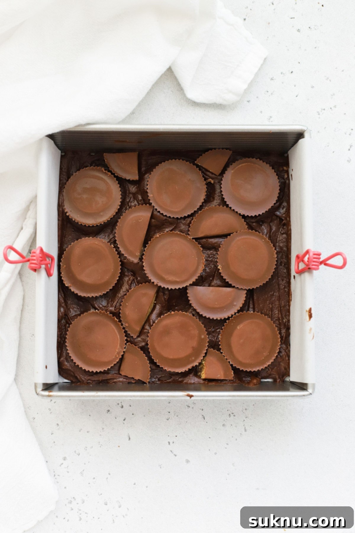 A baker adding peanut butter cups to a pan of rich gluten-free brownie batter, highlighting the sharp corners of an 8x8 metal pan.