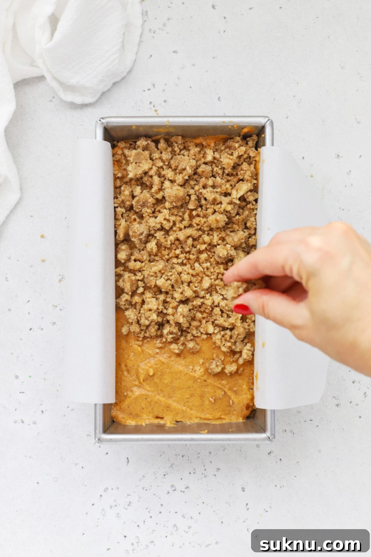 Adding a crumble streusel topping to a beautiful gluten-free cinnamon swirl pumpkin bread in a light-colored loaf pan.