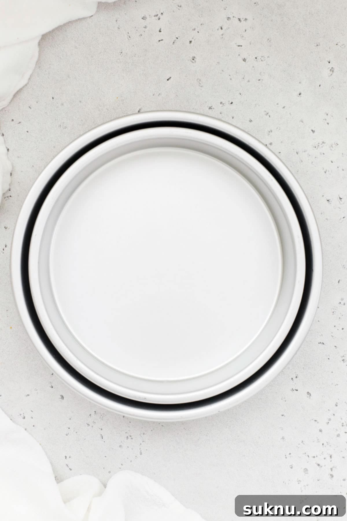 A stack of 8-inch and 9-inch light-colored metal round cake pans, ready for baking magnificent layer cakes.