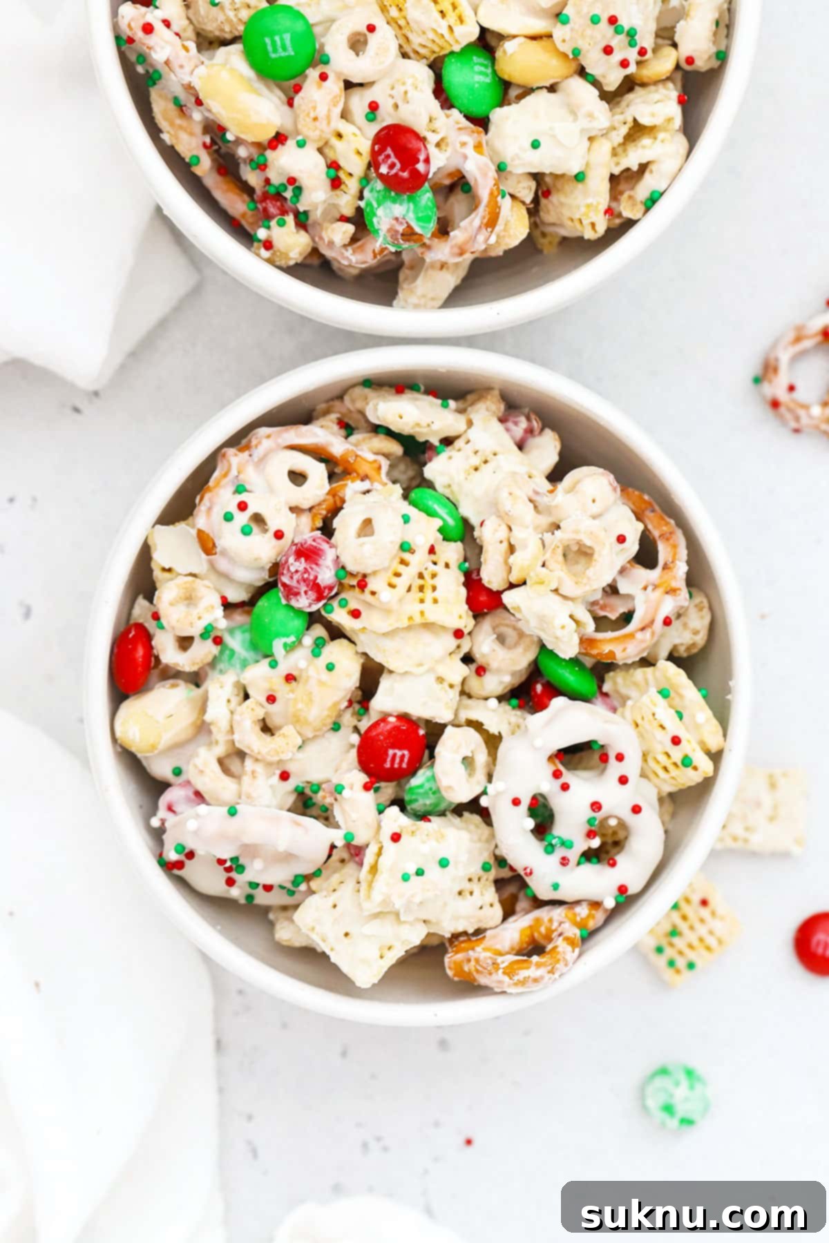 Two white bowls of gluten-free christmas chex mix with m&ms and pretzels