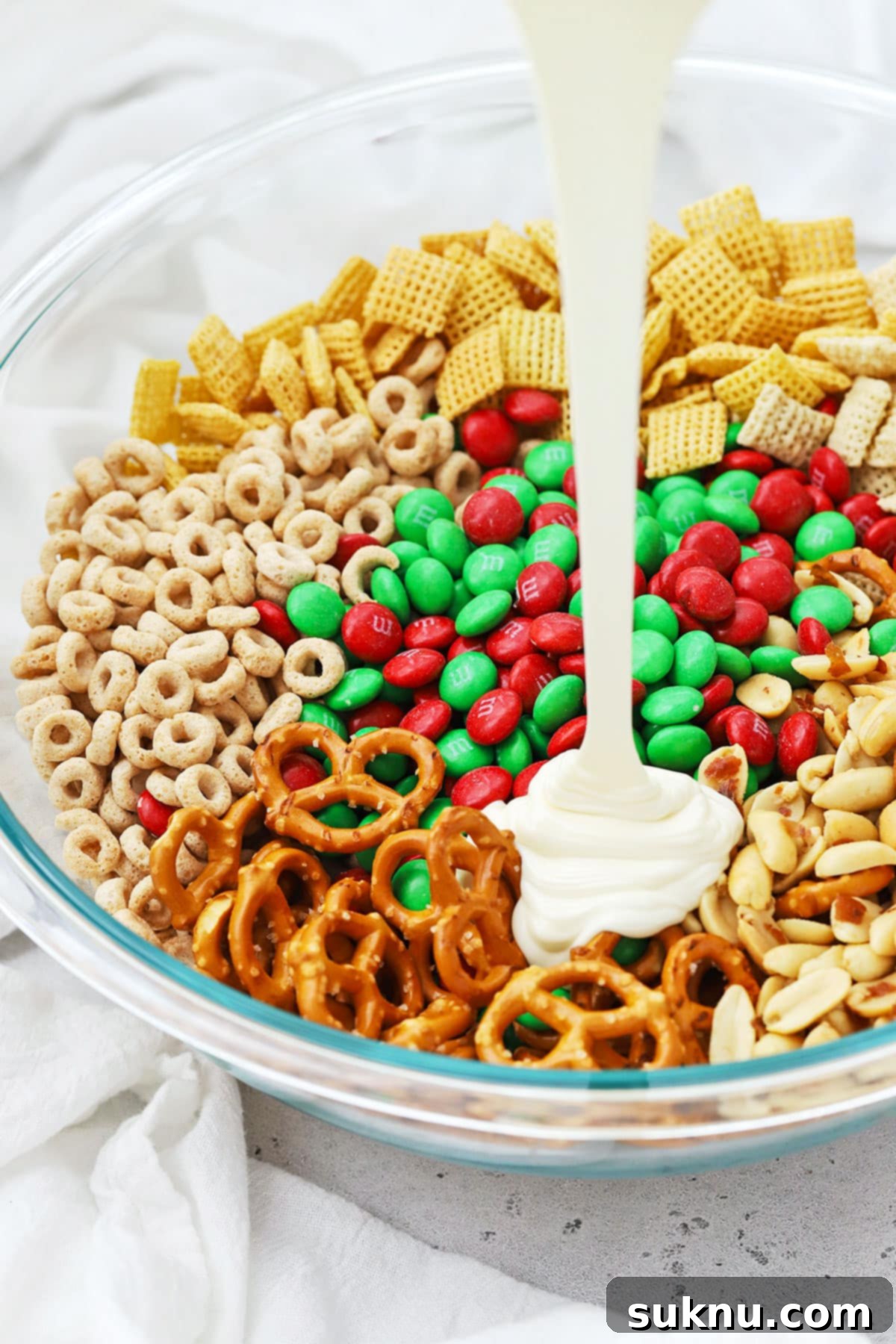 Pouring melted vanilla candy melts over cereal, pretzels, m&ms, and peanuts