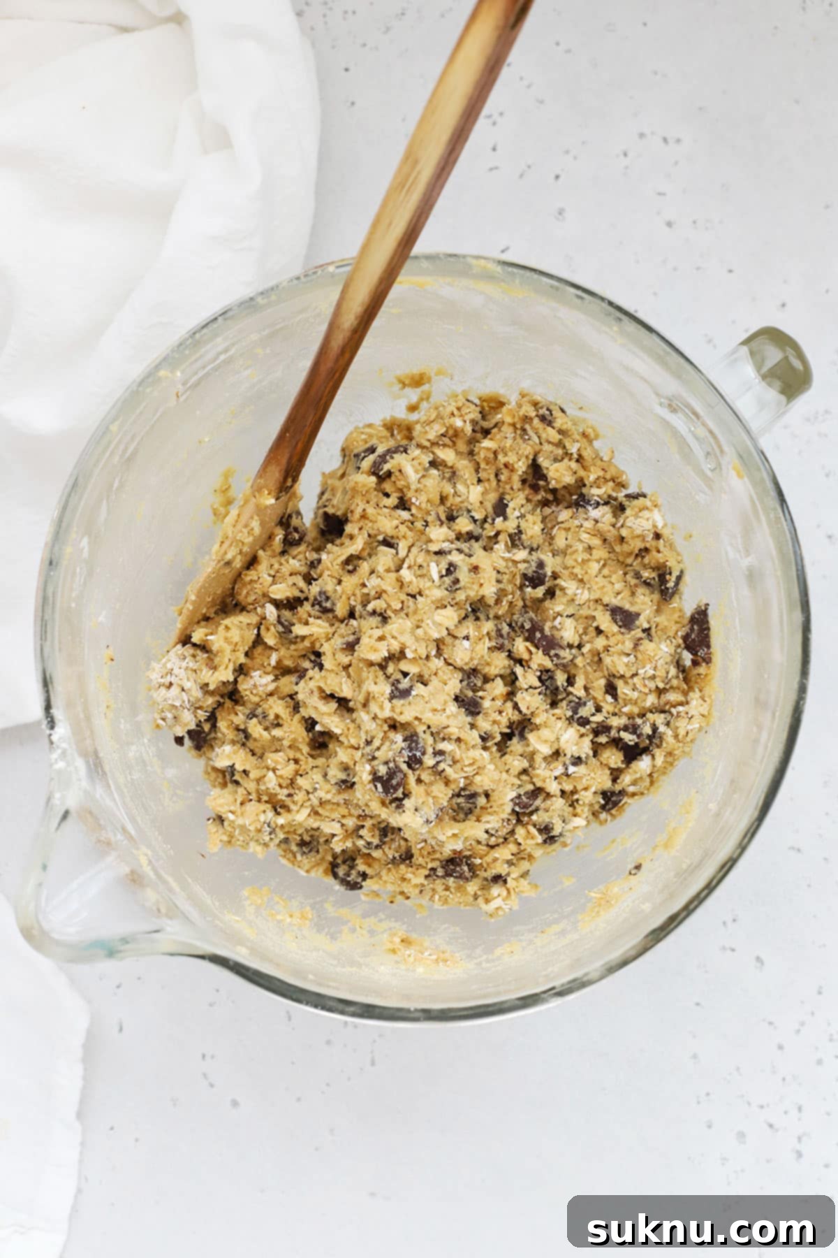 Fully mixed gluten-free oatmeal chocolate chip cookie dough resting in a clear glass bowl