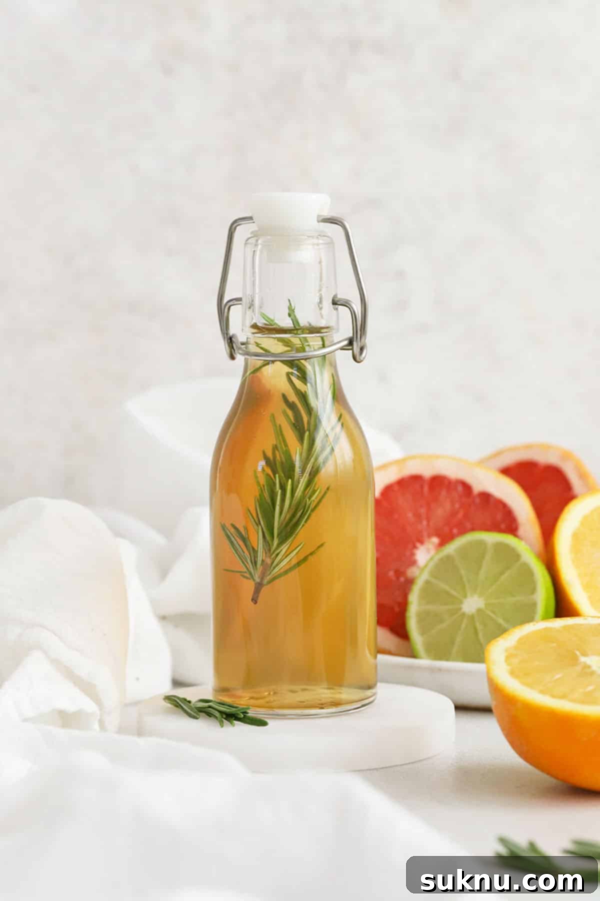 A small glass bottle of rosemary simple syrup with a plate of colorful citrus in the background, hinting at fresh flavors for cocktails and mocktails.