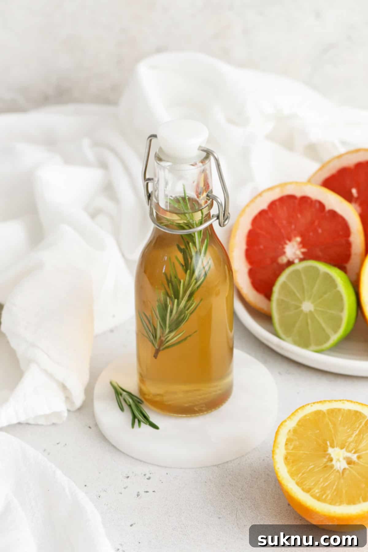 A small glass bottle of rosemary simple syrup sits invitingly on a plate with colorful citrus slices in the background, symbolizing the fresh, vibrant potential of this homemade infusion.