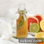 A small glass bottle of rosemary simple syrup with a plate of colorful citrus in the background, a beautiful visual for a homemade infusion.
