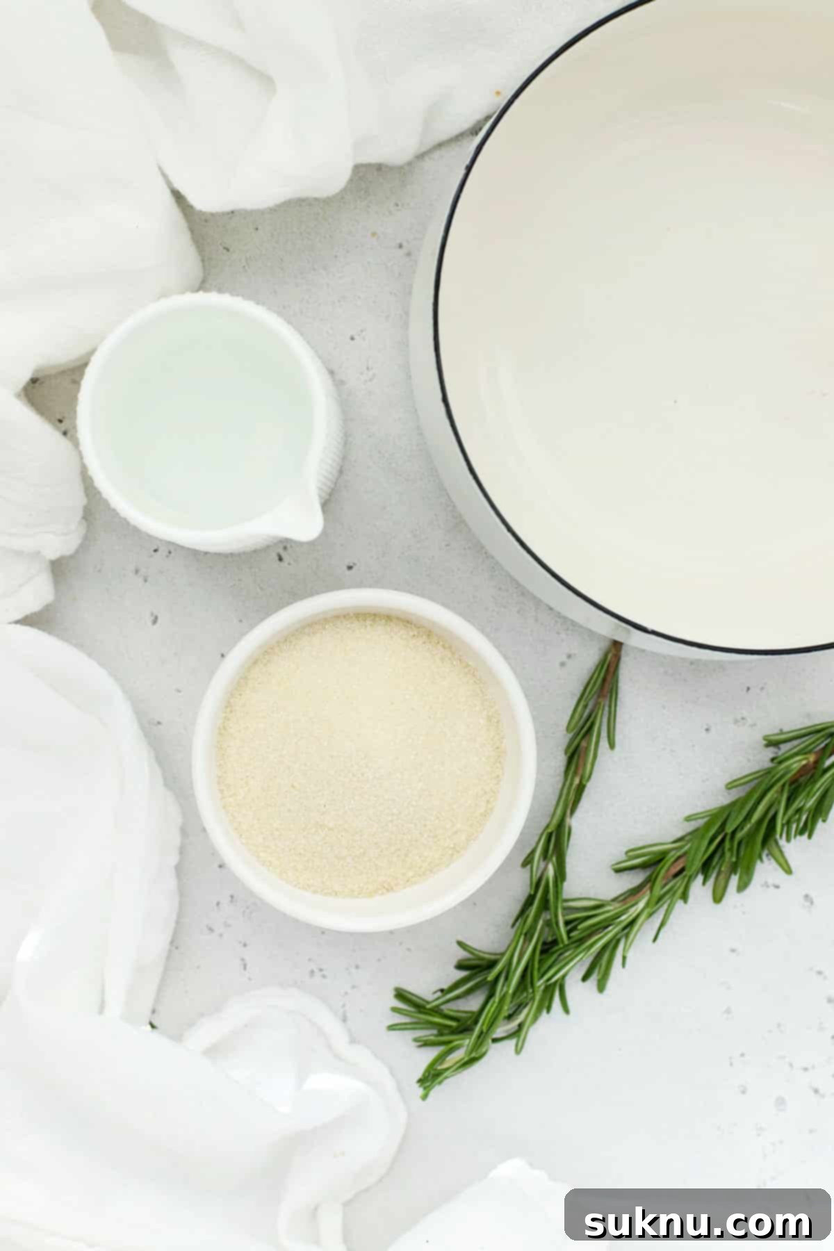 Ingredients for rosemary simple syrup laid out on a clean white background, highlighting the freshness of the rosemary sprigs and simplicity of the components.