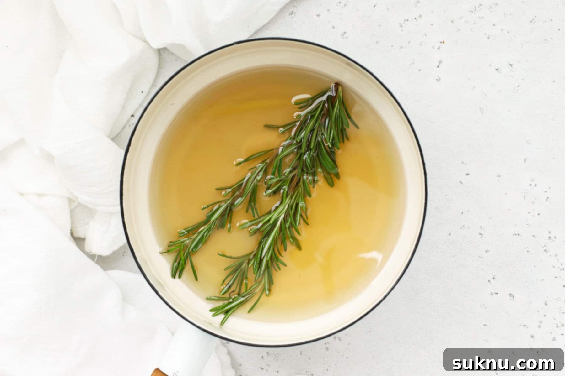 Steeping fresh rosemary in simple syrup in a saucepan on the stovetop, showing the gentle infusion process that creates the aromatic flavor.