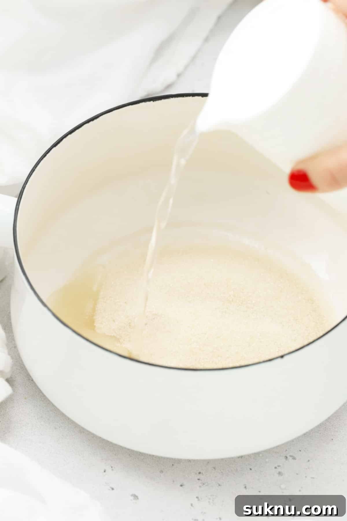 Adding water to a saucepan with sugar, the first step in creating rosemary simple syrup, showing the clear ingredients before heating.