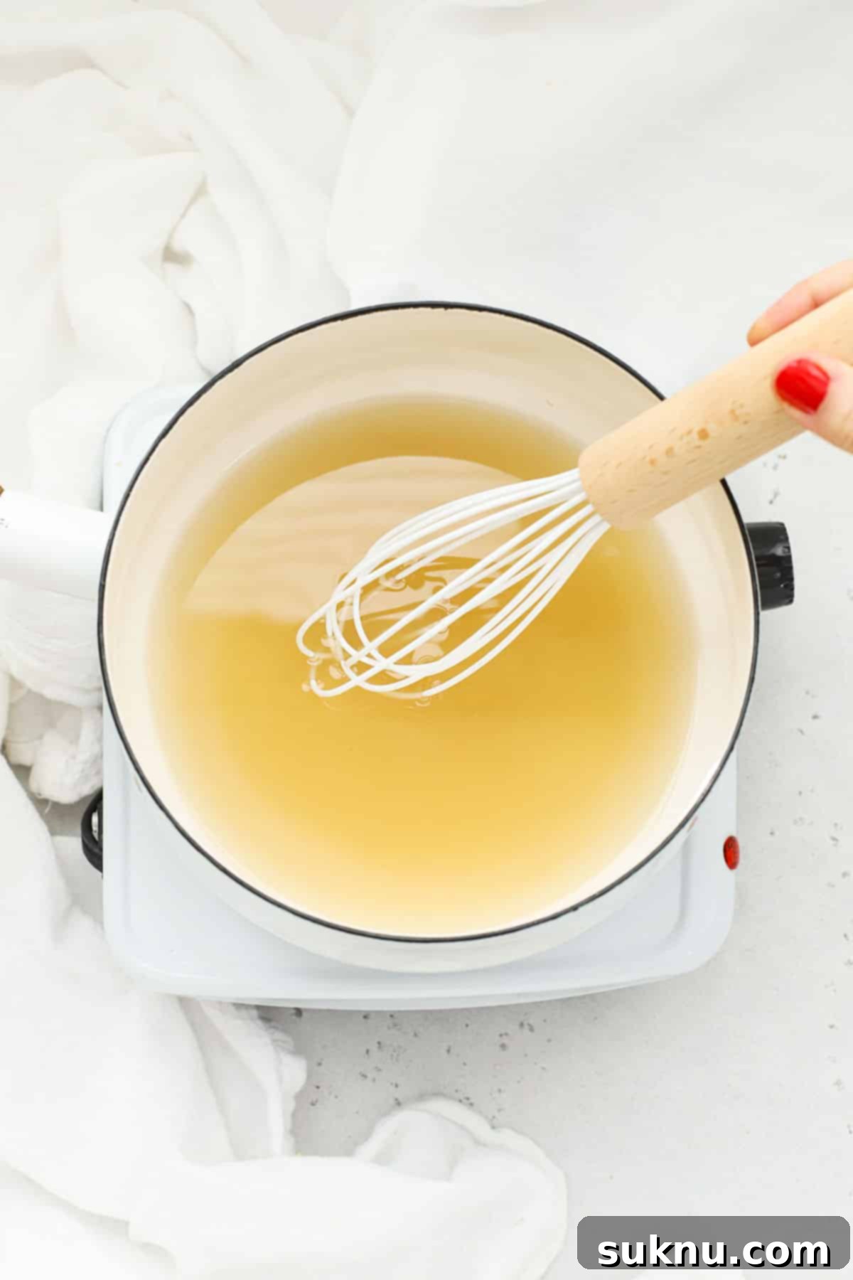 Dissolving sugar in water in a white saucepan over gentle heat, demonstrating the transformation of granular sugar into a clear, unified syrup.