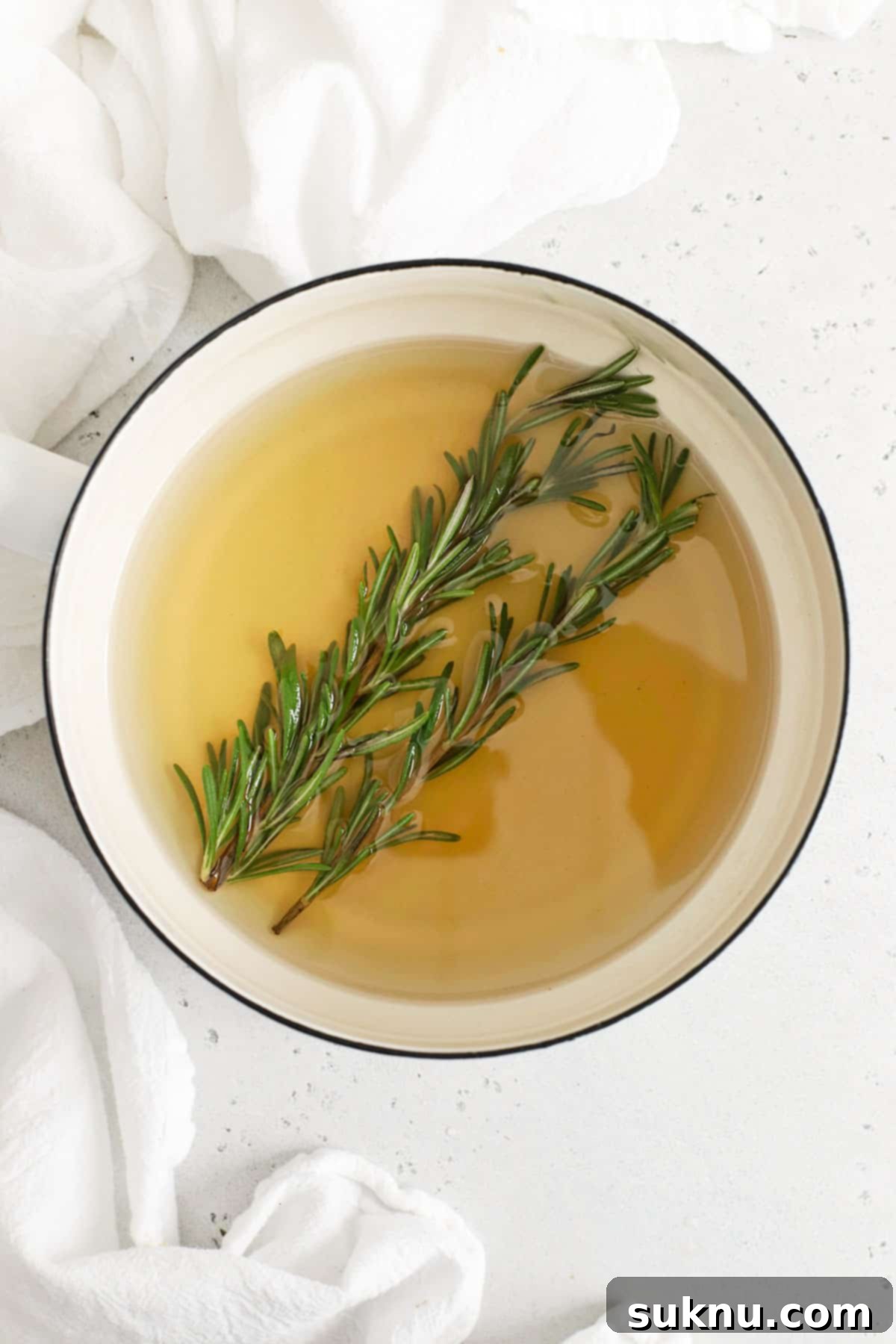 Steeping fresh rosemary sprigs in warm simple syrup, illustrating the infusion process where the herb's flavor permeates the liquid.