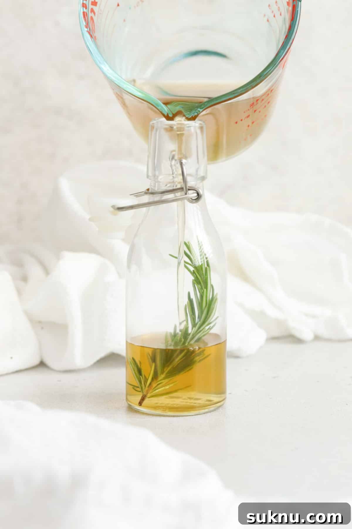 Pouring finished rosemary simple syrup into a jar with a fresh sprig of rosemary for garnish, showcasing the final product ready for use.
