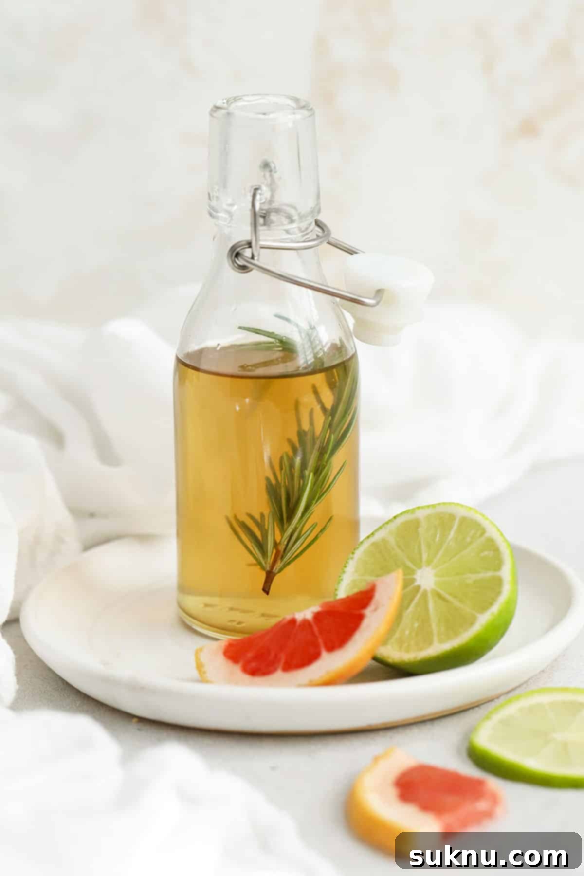 A small bottle of rosemary simple syrup rests on a plate with fresh grapefruit and lime slices, emphasizing its use in citrus-based drinks and its refreshing qualities.