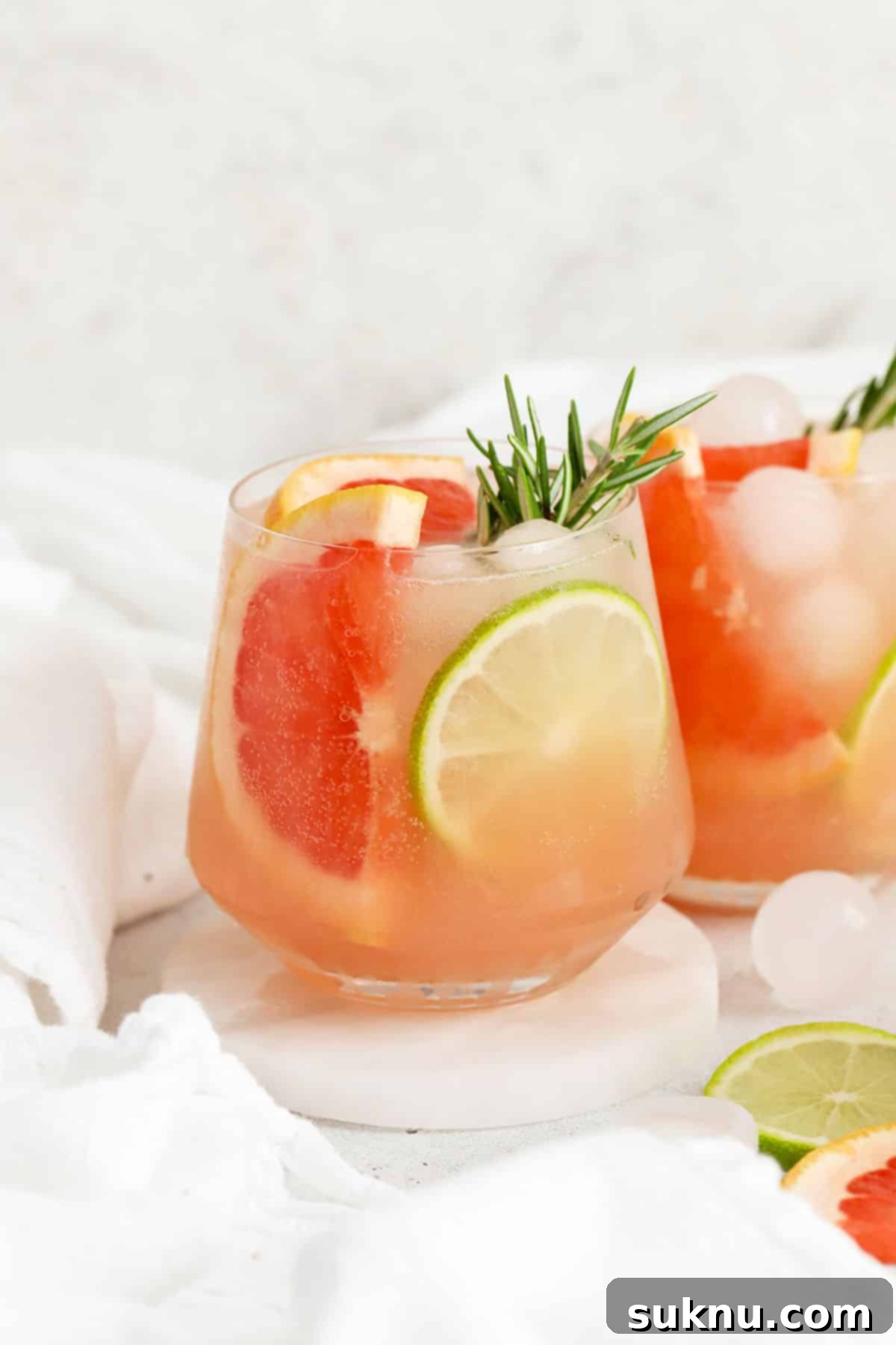 Two vibrant grapefruit mocktails garnished with grapefruit wedges, lime slices, and fresh rosemary sprigs, illustrating a delicious application of rosemary simple syrup in refreshing non-alcoholic drinks.