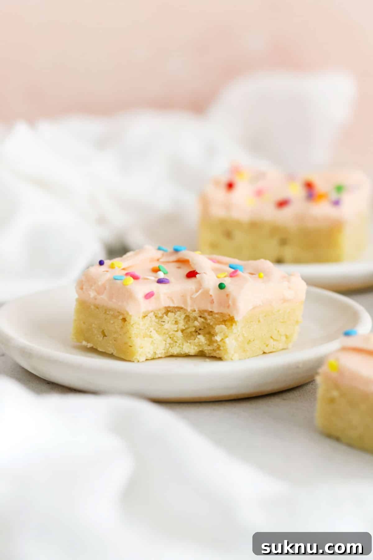Perfect Gluten-Free Sugar Cookie Bars 3 Delicious gluten-free sugar cookie bars topped with light pink frosting and colorful sprinkles, arranged beautifully on white plates.