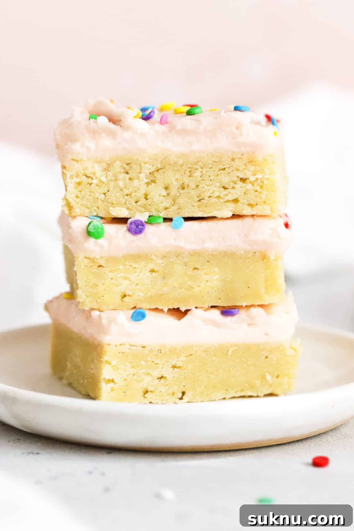 Perfect Gluten-Free Sugar Cookie Bars 9 Three perfectly frosted gluten-free sugar cookie bars with pink frosting and sprinkles, stacked on a pristine white plate, ready to be enjoyed.