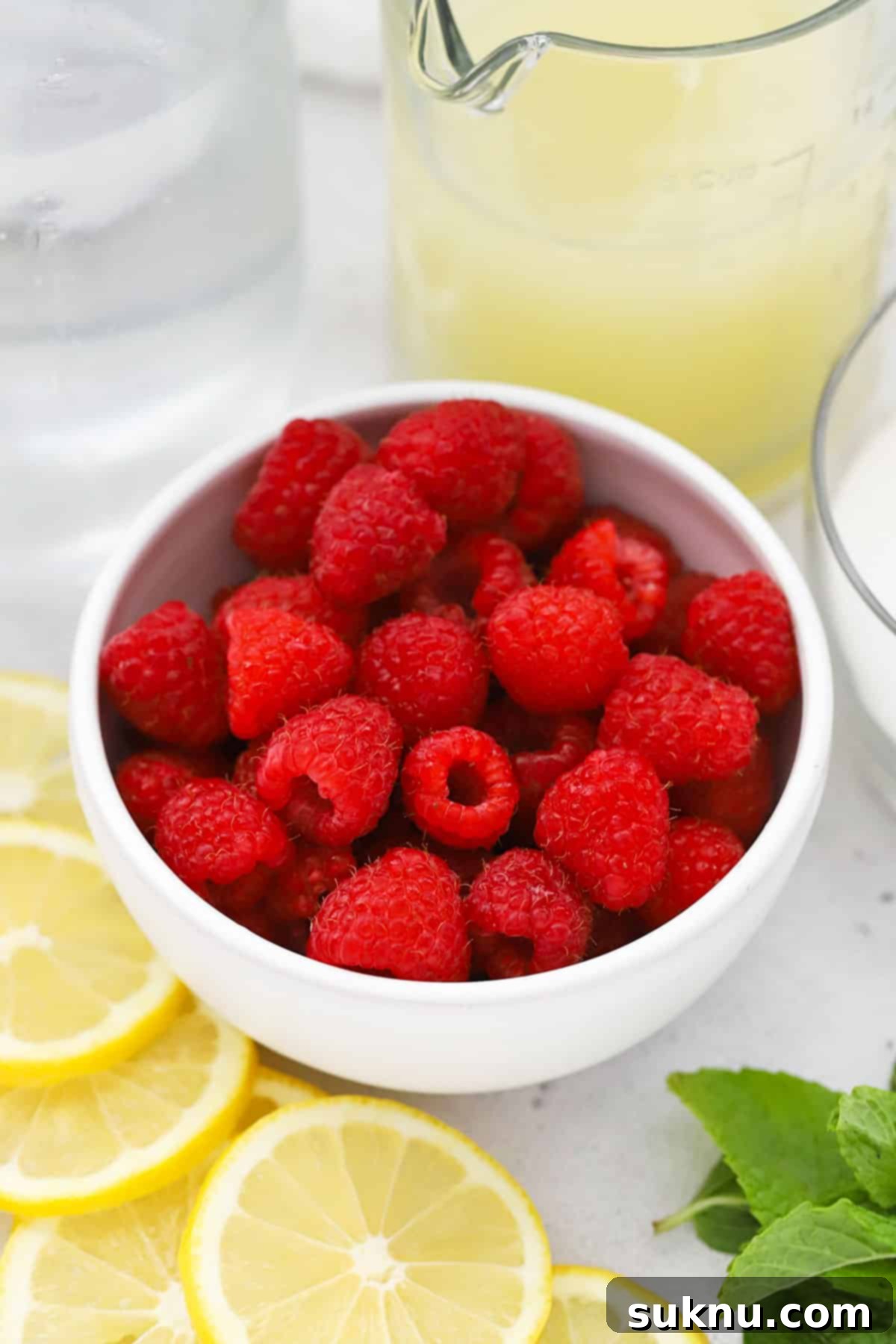 Perfect Raspberry Lemonade 3 Ingredients for homemade raspberry lemonade, including fresh lemons, raspberries, sugar, and a pitcher of water