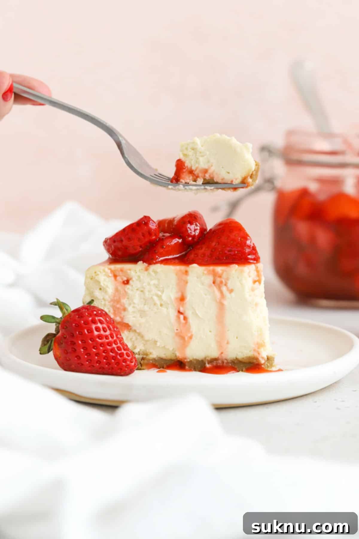 A slice of gluten-free strawberry cheesecake with strawberry topping on a white plate