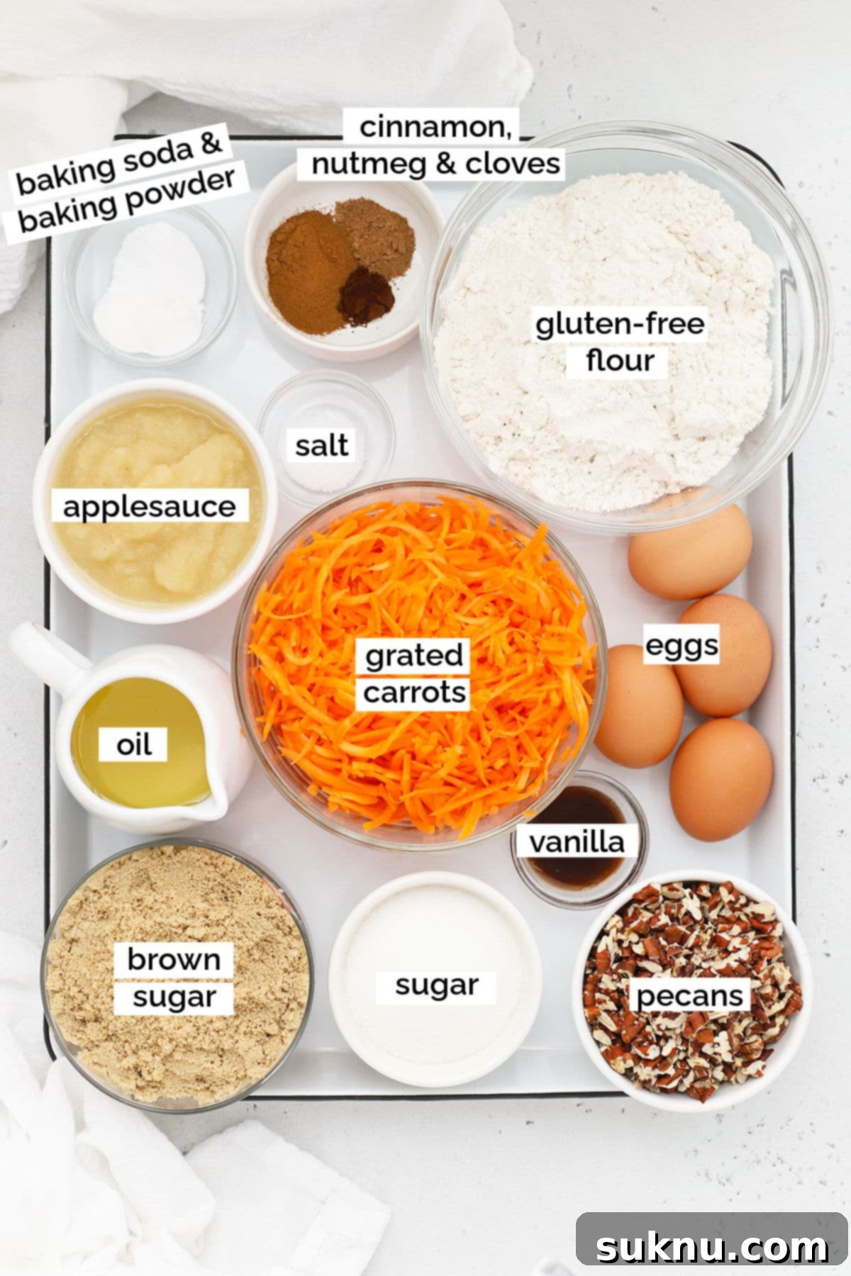 Moist Gluten Free Carrot Cake 3 A vibrant display of fresh ingredients for gluten-free carrot cake, including grated carrots, flour, eggs, spices, and a bowl of unsweetened applesauce.