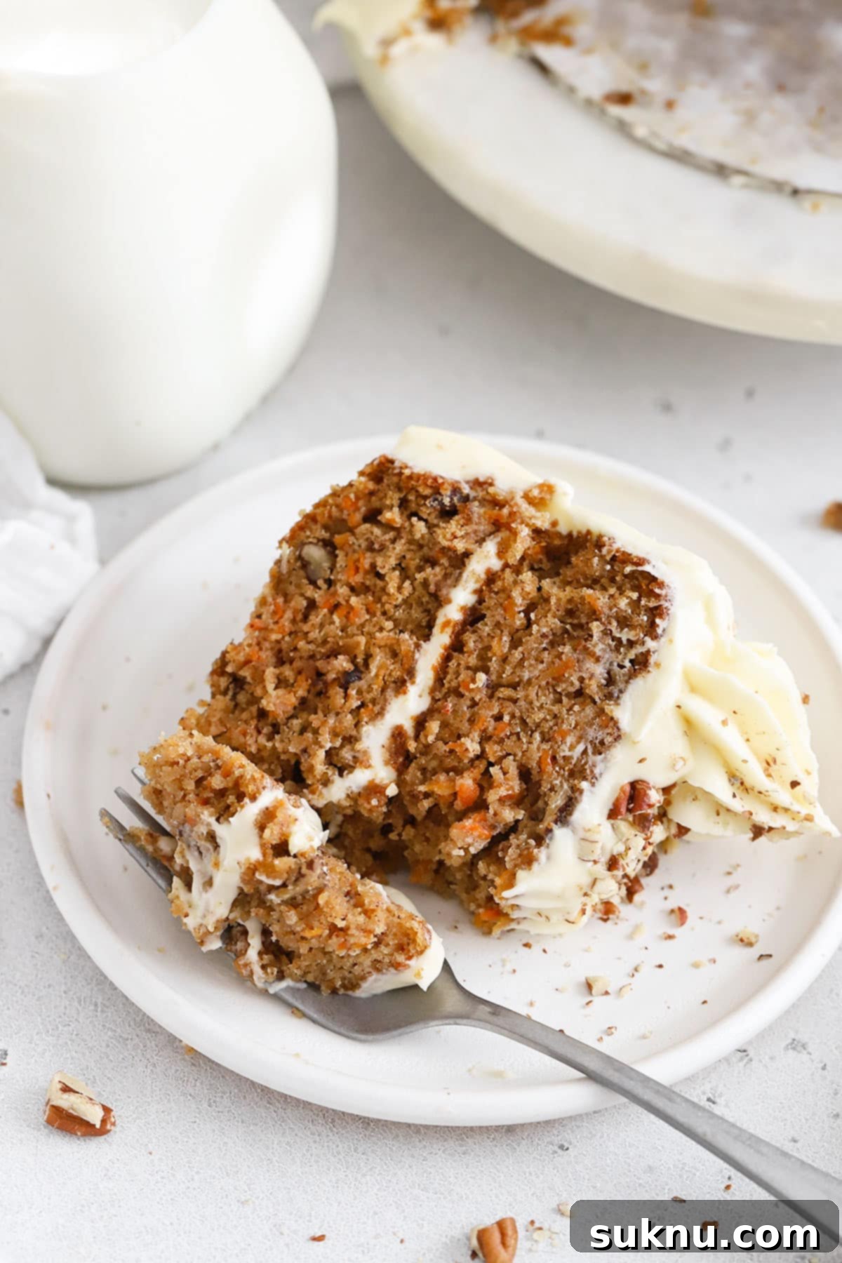 Moist Gluten Free Carrot Cake 8 A fork gently cutting into a thick slice of two-layer gluten-free carrot cake, highlighting its moist interior, nuts, and creamy frosting.