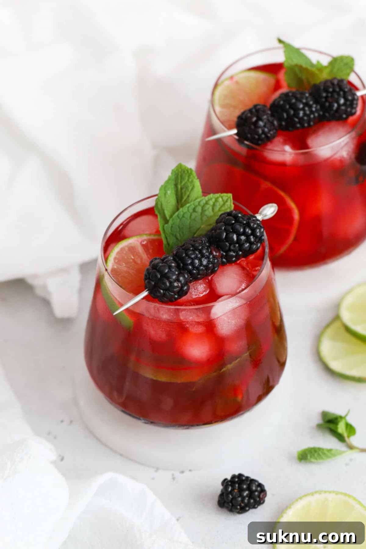 Two glasses of homemade blackberry limeade on white coasters, garnished with fresh blackberries and mint.