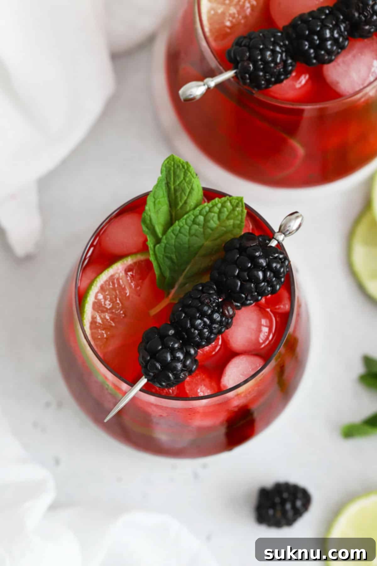 Two glasses of blackberry limeade on white coasters, showcasing beautiful garnishes.