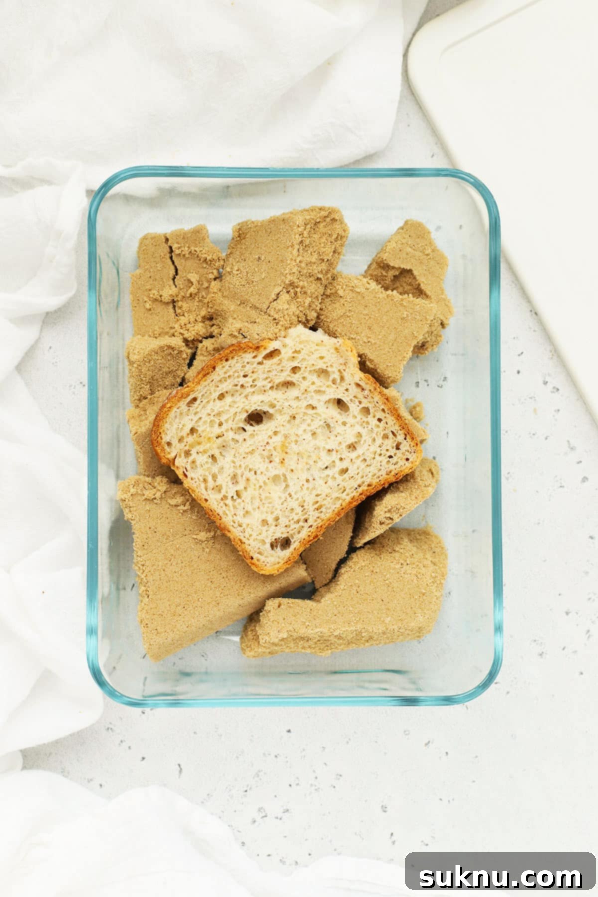 Revive Your Hard Brown Sugar 6 A container of brown sugar with a slice of gluten-free bread resting on top, demonstrating the bread softening method.