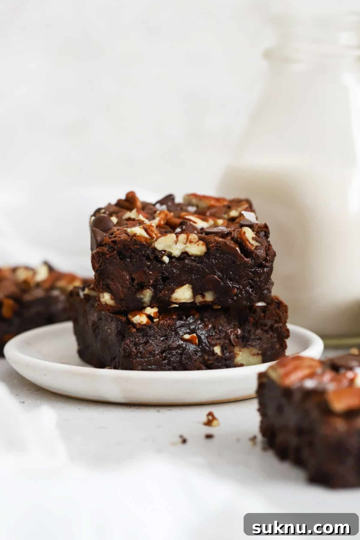 Decadent Gluten-Free Pecan Brownies 7 A stack of three fudgy gluten-free pecan brownies on a white plate, showcasing their thick, rich layers.